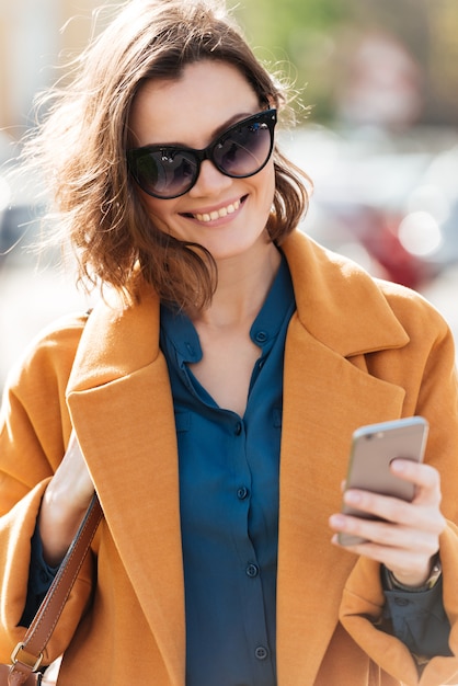 Donna sorridente felice in occhiali da sole e cappotto