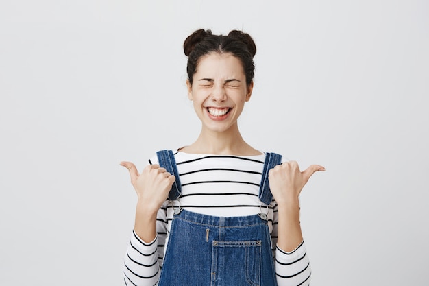 Happy smiling woman with closed eyes pointing fingers left and right