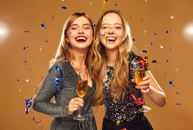 Free photo happy smiling women in stylish glamorous dresses with champagne glasses under confetti