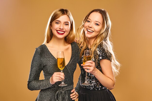 Счастливые улыбающиеся женщины в стильных гламурных платьях с бокалами для шампанского
