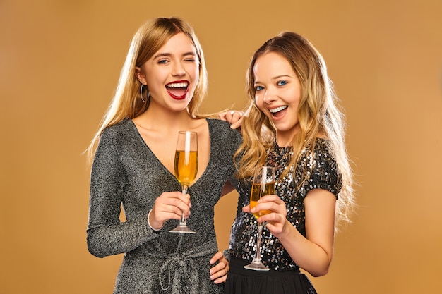 Счастливые улыбающиеся женщины в стильных гламурных платьях с бокалами для шампанского