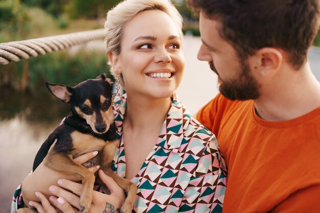 Free photo happy smiling young couple hugging their dog on bridge