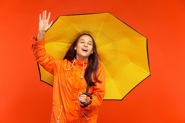 The happy smiling young girl posing at studio in autumn orange jacket isolated on orange wall