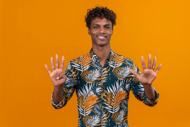 Happy and smiling young handsome dark-skinned man with curly hair in leaves printed shirt  while showing with fingers number ten 