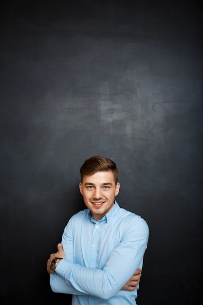 happy smiling young man in blue shirt over blackboard