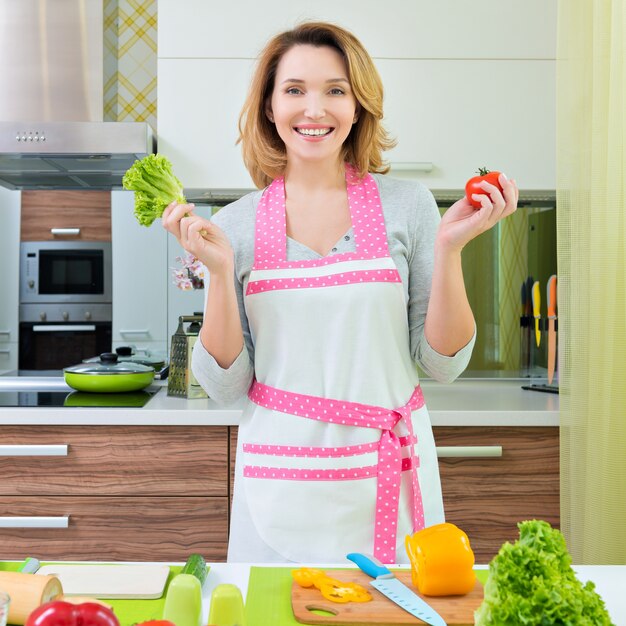 Happy smiling young woman cooking a salad at the kitchen.