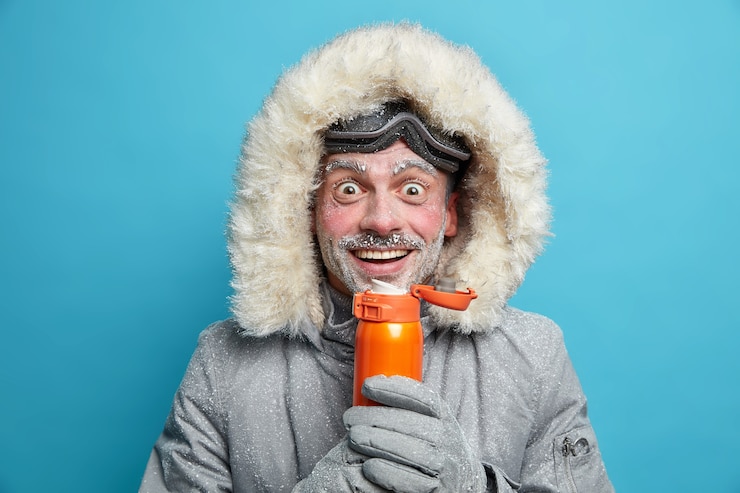 Free Photo happy snow man enjoys extreme sport during cold frosty day in mountains wears ski goggles and jacket warms with hot beverage has white frost on face. hiking mountaineering active rest concept