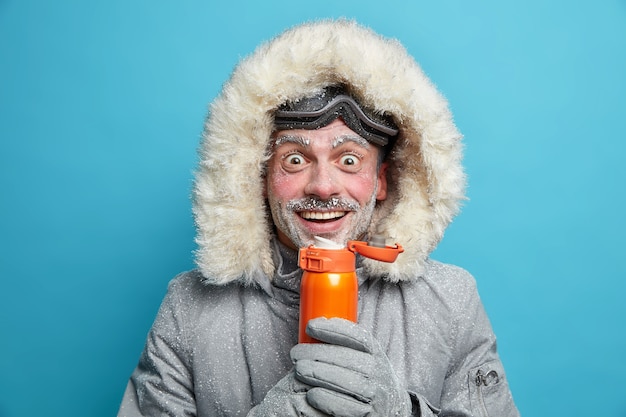 L'uomo della neve felice gode di sport estremi durante una fredda giornata gelida in montagna indossa occhiali da sci e la giacca si scalda con una bevanda calda ha il gelo bianco sul viso. escursionismo alpinismo concetto di riposo attivo