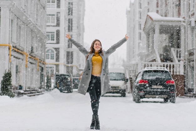 Happy snowing winter time in big city of pretty girl enjoying snowfall on street. True positive emotions, holding hands above,