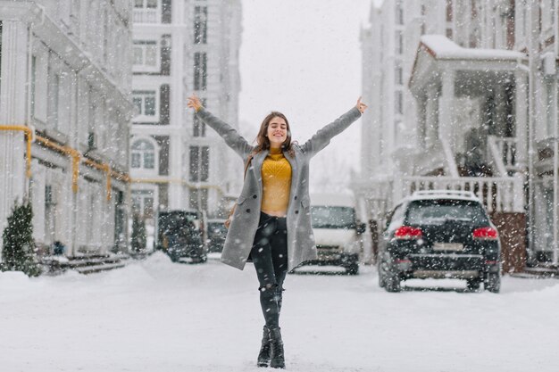 Счастливое снежное зимнее время в большом городе красивая девушка, наслаждающаяся снегопадом на улице. Настоящие положительные эмоции, держась за руки вверху,