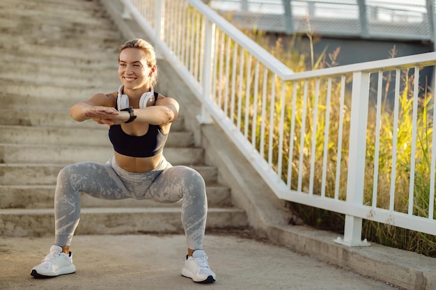 Happy sportswoman doing squats while working out outdoors