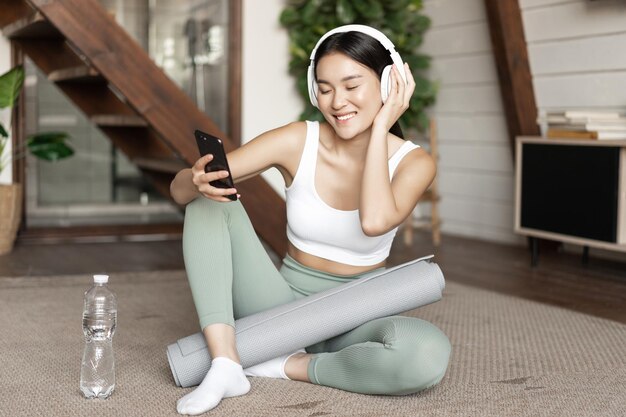 Free Photo happy sporty girl sitting on floor at home and taking selfie during workout wearing headphones and h...