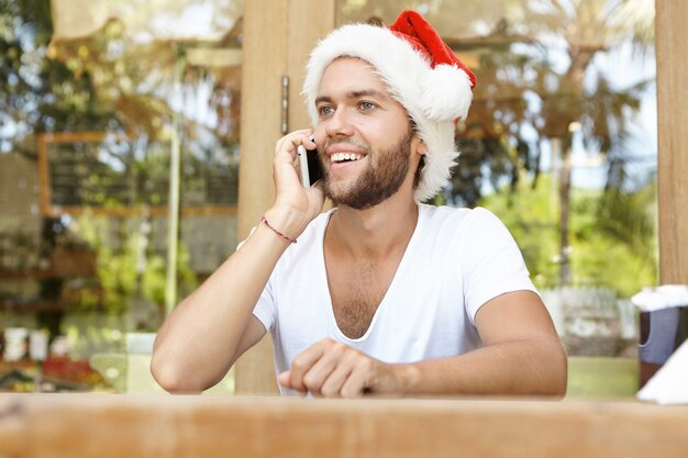 Happy student wearing Santa Claus hat talking on cell phone