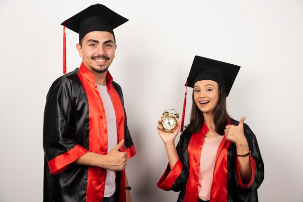 Happy students in gown with clock standing on white.