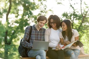 Happy students sitting and studying outdoors while using laptop