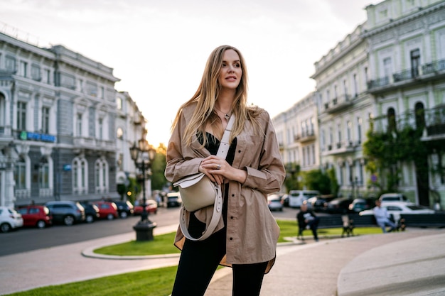 Счастливая стильная блондинка позирует на улице, путешествуя по Европе летом