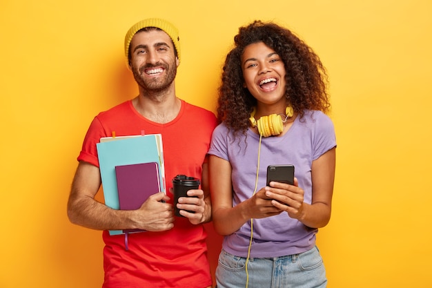 happy stylish couple posing against the yellow wall with gadgets