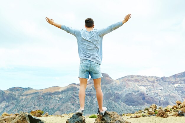 캐주얼 소식통 옷을 입고 행복 세련된 남자 태양에 제기 손으로 산의 절벽에 서서 성공을 축하