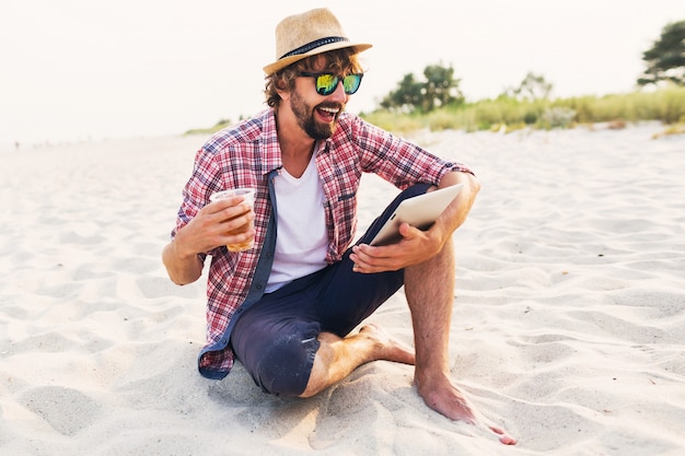 Foto gratuita felice uomo elegante utilizzando tablet e bere birra sulla spiaggia