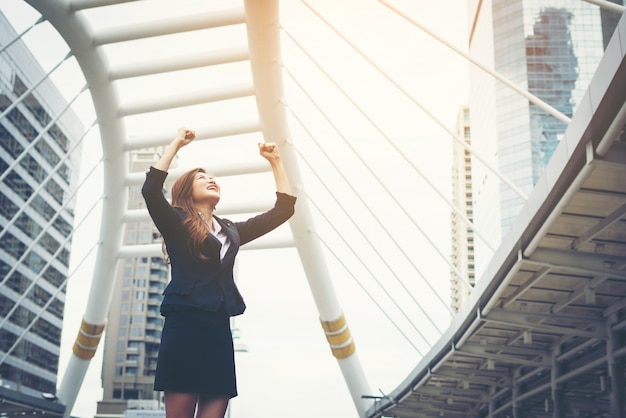 Happy Success Businesswoman overlooking into the city center hands raised.