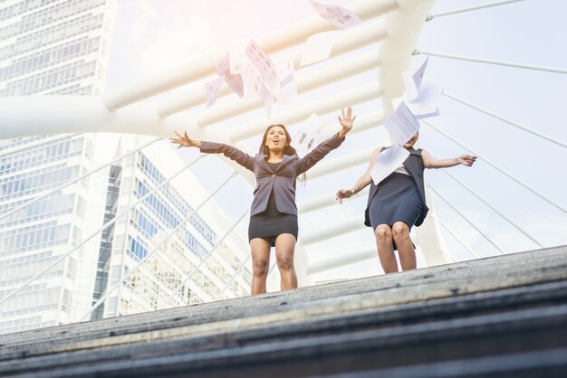 Happy Success Businesswomen overlooking jummping into the city center hands raised.