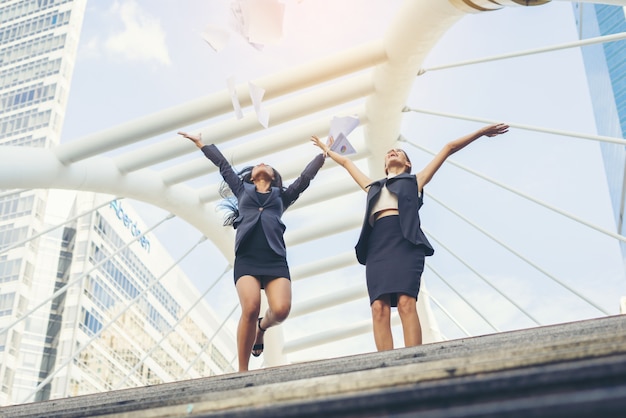 Happy Success Businesswomen overlooking jummping into the city center hands raised.