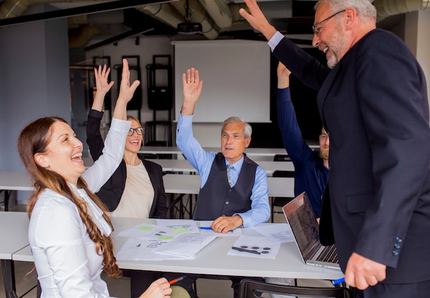 Happy successful businesspeople raising their hands in the board meeting