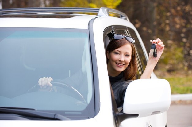 新しい車からの鍵を持つ幸せな成功した女性