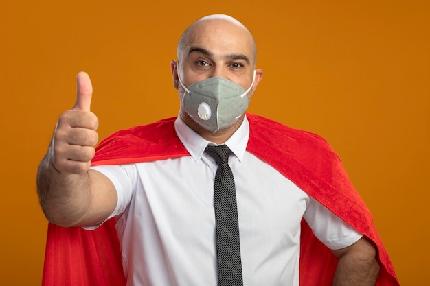 Foto gratuita felice uomo d'affari super eroe in maschera facciale protettiva e mantello rosso che mostra i pollici in su