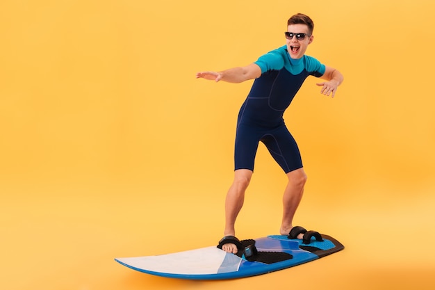 Happy surfer in wetsuit and sunglasses using surfboard like on wave