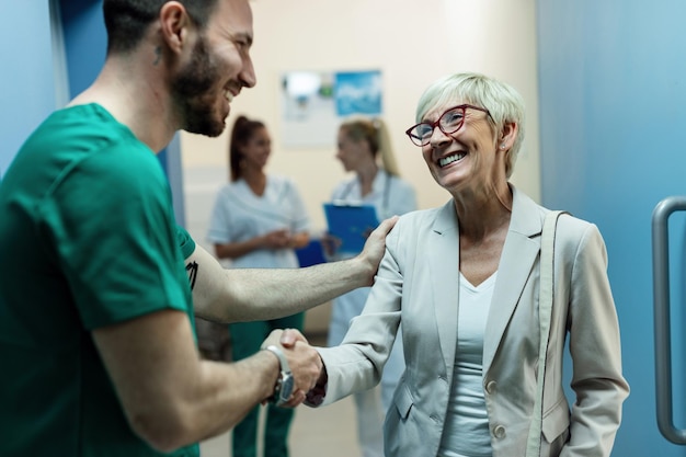 Happy surgeon and senior woman handshaking while greeting in a lobby at clinic Focus is on woman