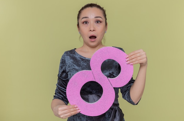 Happy and surprised asian woman holding number eight made