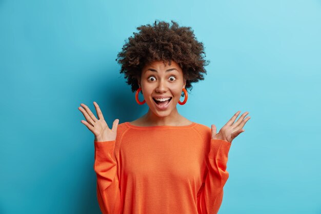 Happy surprised attractive Afro American woman raises hands reacts on awesome unexpected relevation
