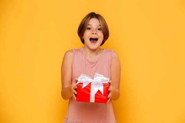 Happy surprised girl holding red present isolated over yellow