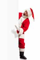 Free photo happy surprised santa claus pointing on blank advertisement banner background with copy space. smiling senior man showing at white blank of empty poster