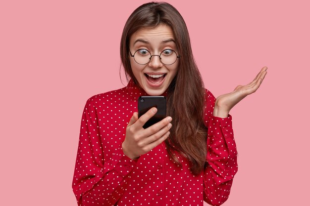 Довольная и удивленная общительная дама позитивно смотрит на экран мобильного телефона, получает хорошие новости, использует современные технологии для онлайн-общения.