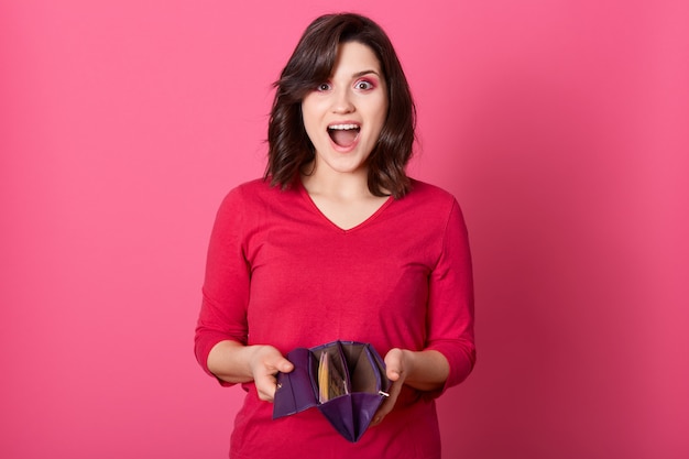 Free photo happy surprised woman holding wallet full of money, win big sum of money, standing with widely opened mouth and excited facial expression, lady wearing red shirt.