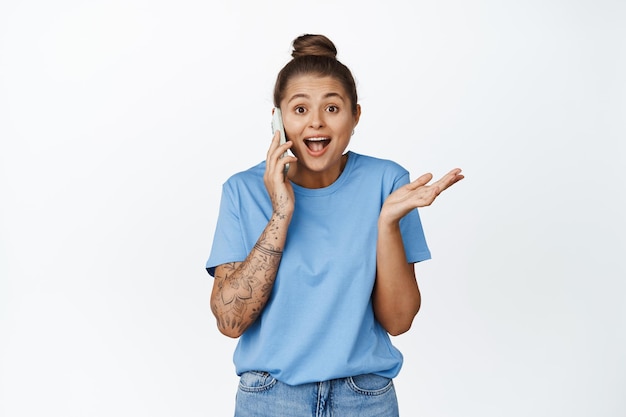 Happy surprised woman talking on mobile phone, receive news on call, smiling excited, standing against white background.