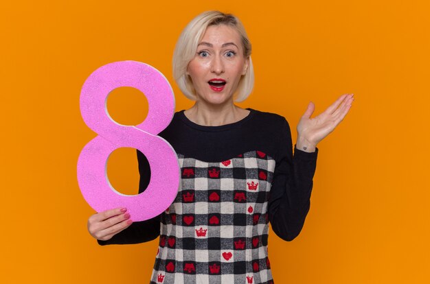 happy and surprised young woman holding number eight made from cardboard