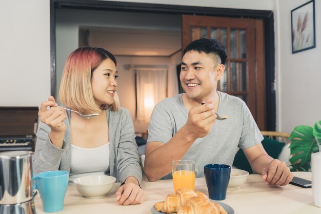 Happy sweet Asian couple having breakfast, cereal in milk, bread and drinking orange juice 