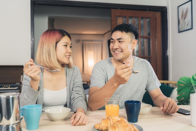 Happy sweet Asian couple having breakfast, cereal in milk, bread and drinking orange juice 