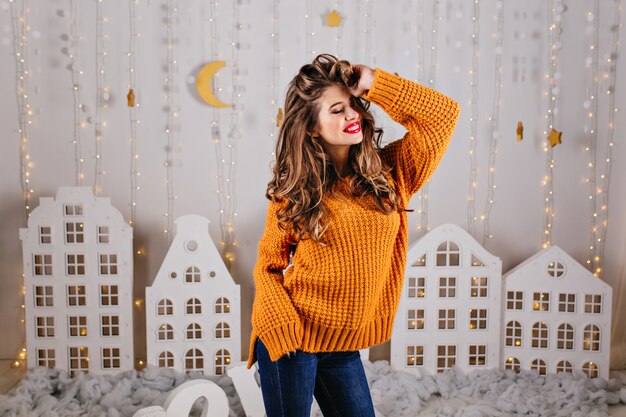 Happy, sweet girl with bright lipstick and beautiful eyes stands over white decorations with festive figures in form of stars