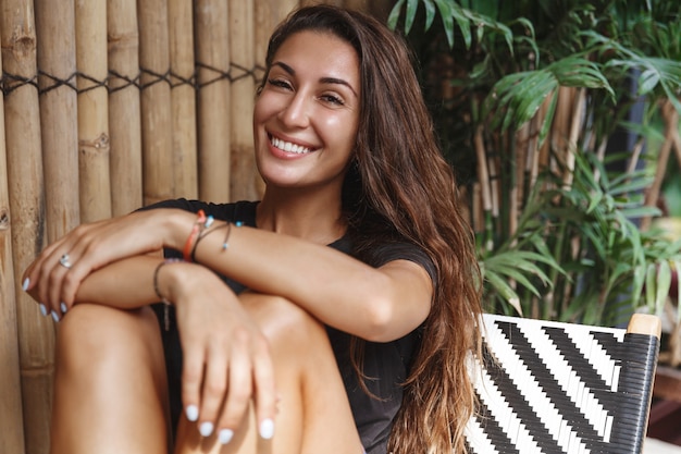 Happy tanned woman relaxing on terrace, smiling at camera.