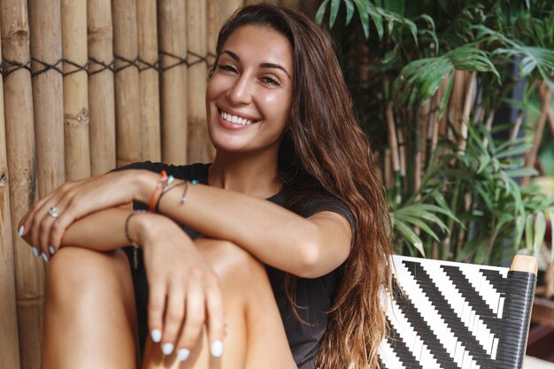 Happy tanned woman relaxing on terrace, smiling at camera.