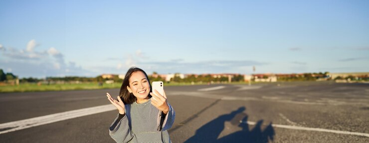 無料Photo 幸せなティーンエイジャーのアジア人女の子は ⁇ スケートボードスケーターに座っている間 ⁇ スマートフォンアプリでセルフィービデオチャットをします ⁇ 