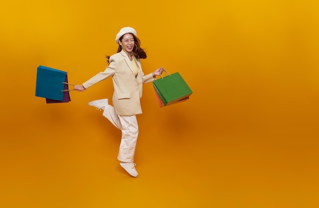 счастливая азиатская женщина-подросток наслаждается покупками, она носит сумки с покупками и прыгает
