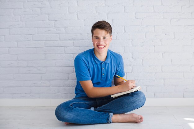 Happy teen boy doing homework on floor