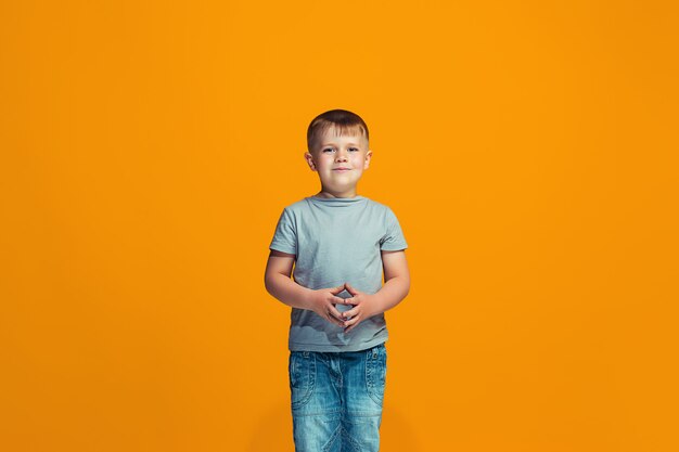 The happy teen boy standing and smiling against orange space.