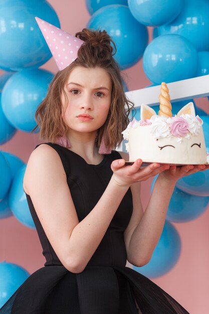 Happy teen girl holding unicorn layered cake decorated with meringues close-up.
