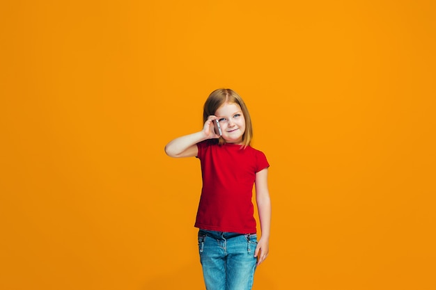 The happy teen girl standing and smiling against orange background.